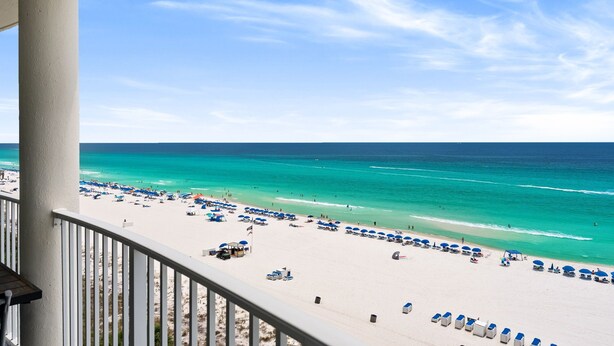 A beach view from a balcony with a railing, beach umbrellas, and lounge chairs. - 8th-Floor Beachfront Condo with Curved Balcony (Panama City Beach)