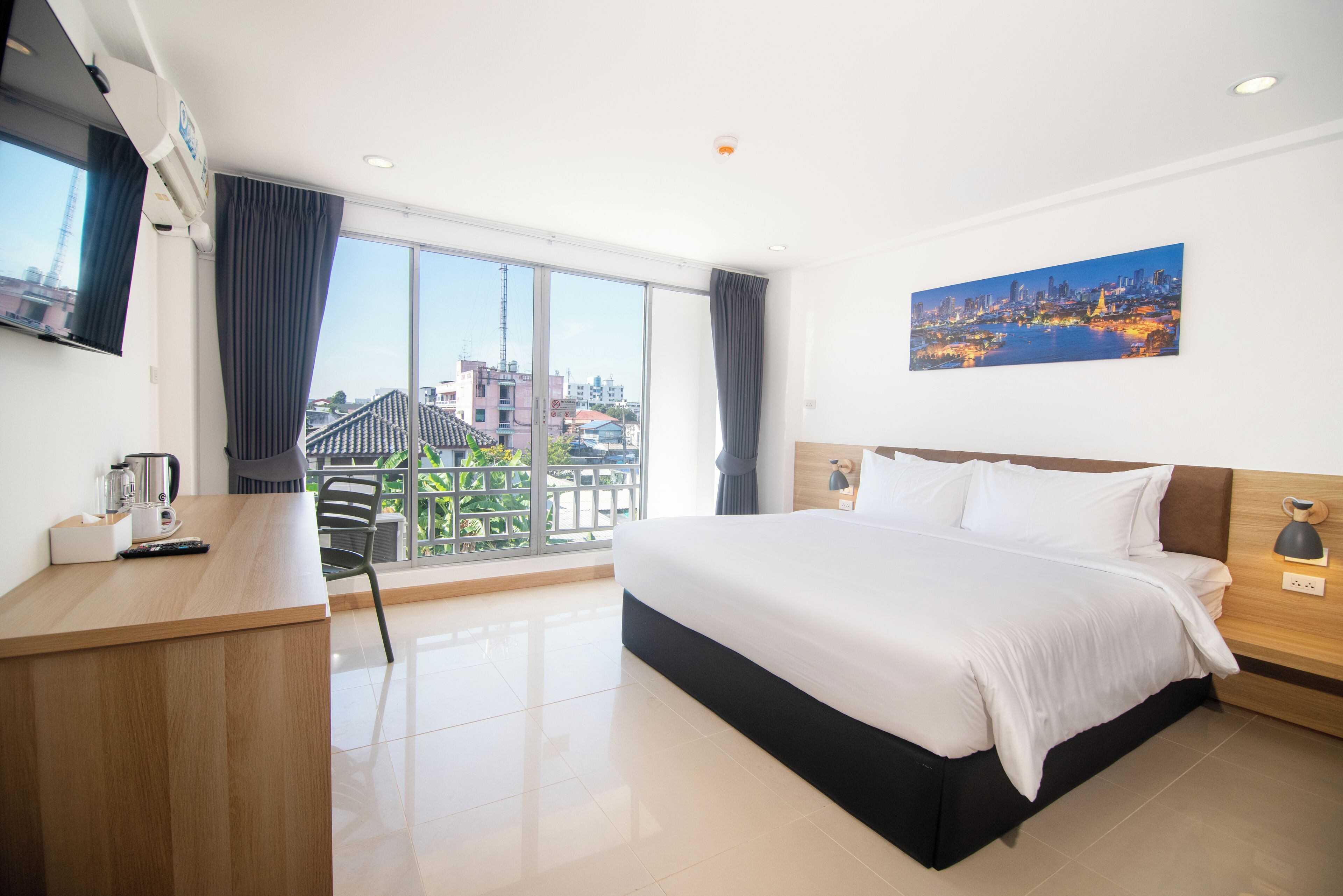 Ein Hotelzimmer mit Bett, Schreibtisch, Stuhl, Fernseher, einem Gemälde und Blick auf die Stadt.