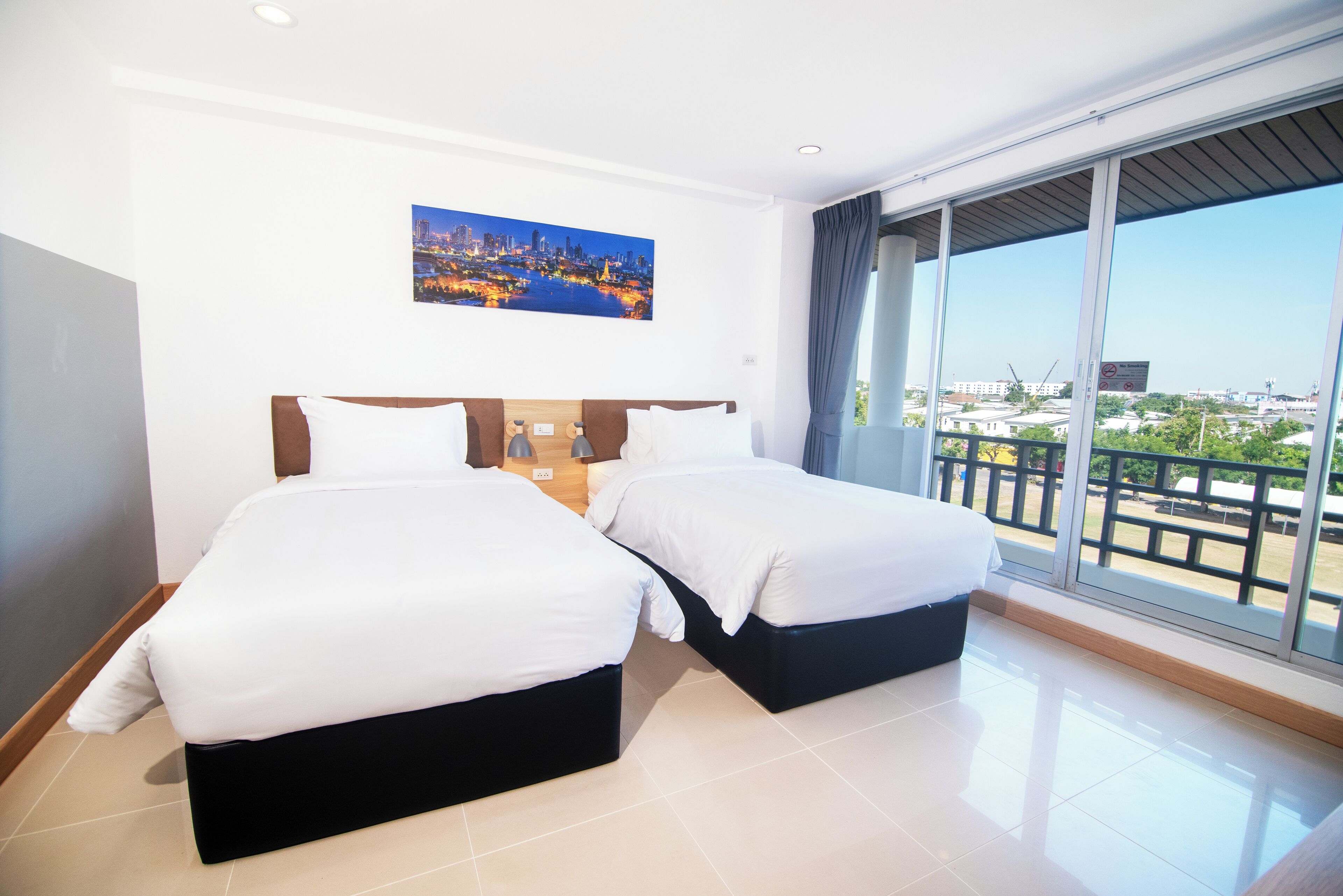 A hotel room with two beds, a cityscape view, and a balcony with a railing.