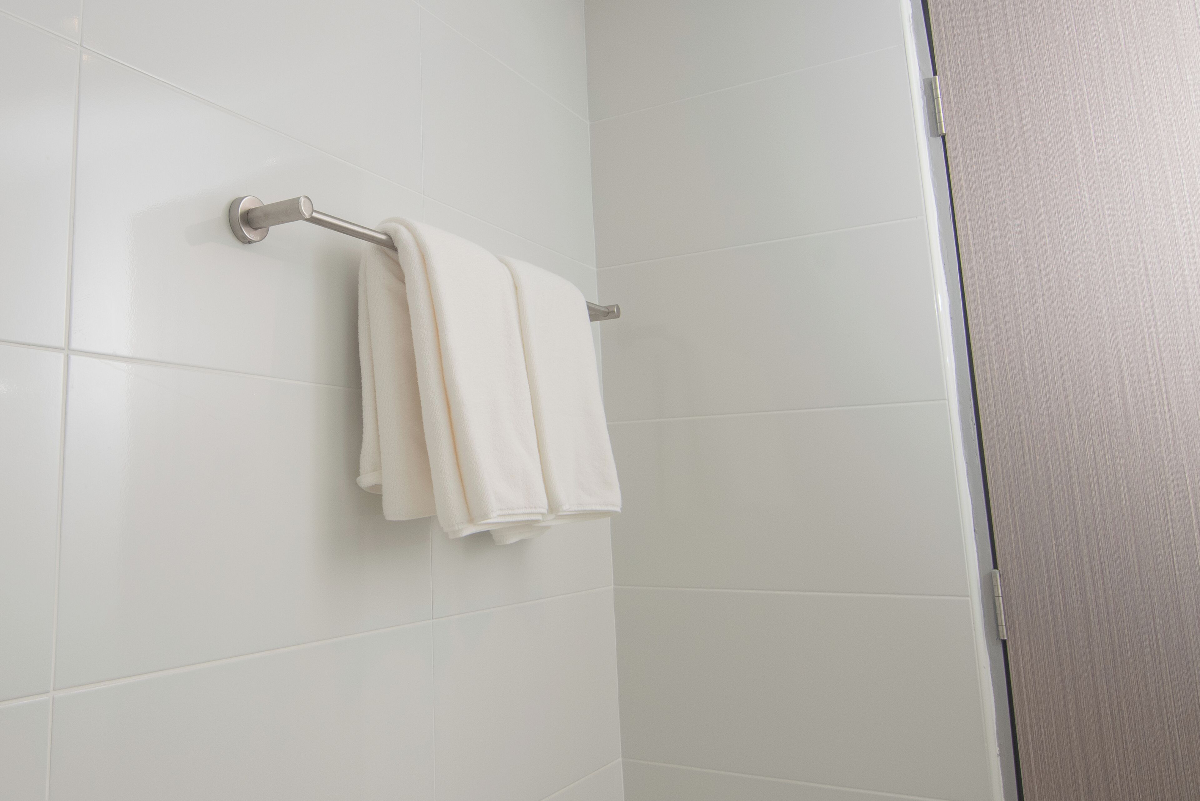 A bathroom with white tiles, a towel rack with two towels, and a door.