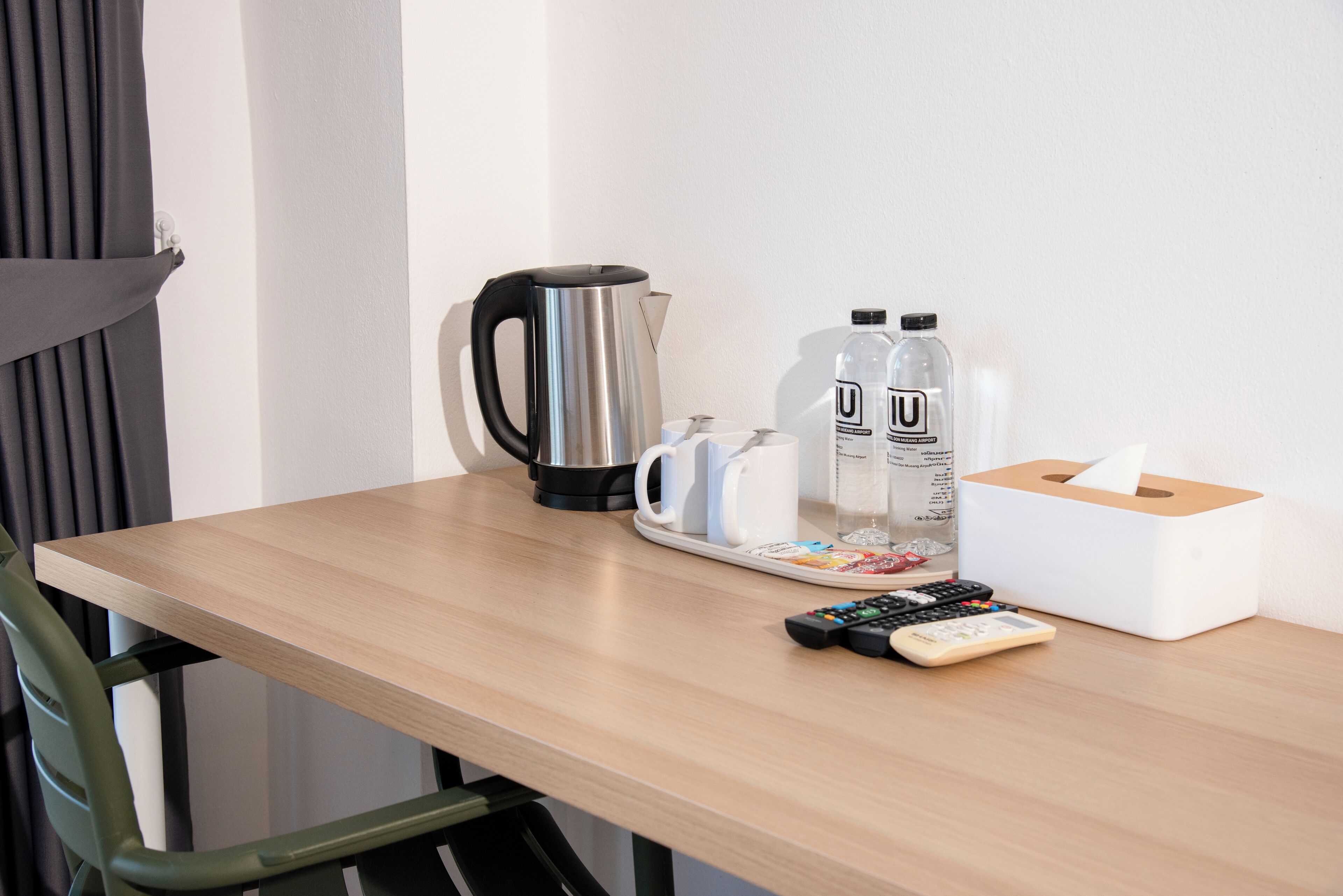 A wooden table with a kettle, two bottles of water, a tissue box, and a remote control.