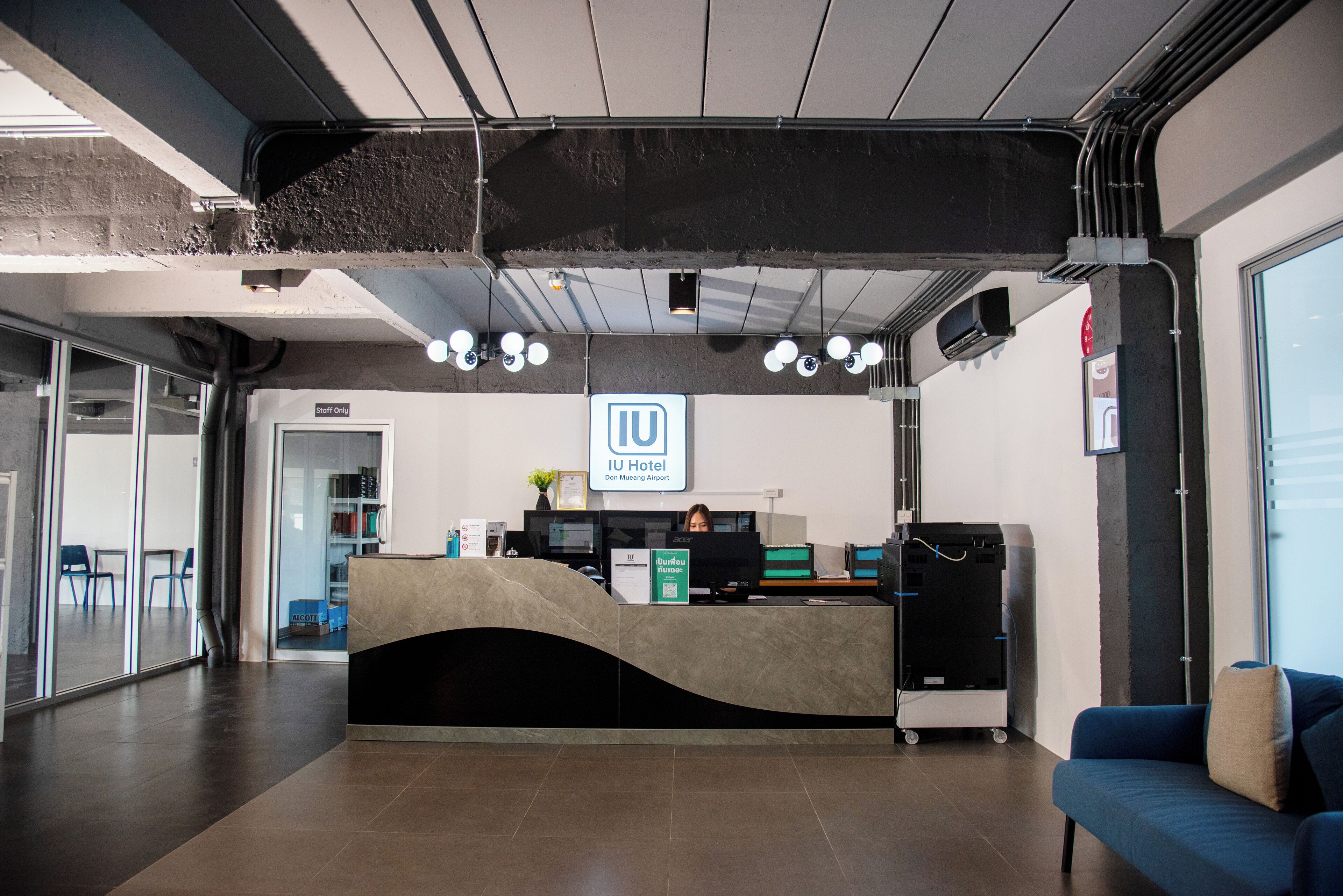 Un comptoir d’accueil d’hôtel au design moderne, une pancarte indiquant que l’accès est réservé au personnel, et une vue sur l’aéroport en arrière-plan.