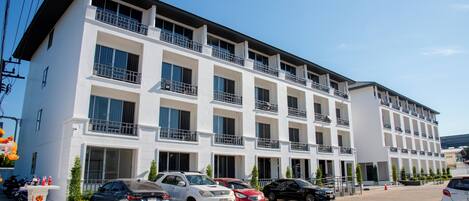 A multi-story hotel with balconies, parking spaces, and a clear sky.
