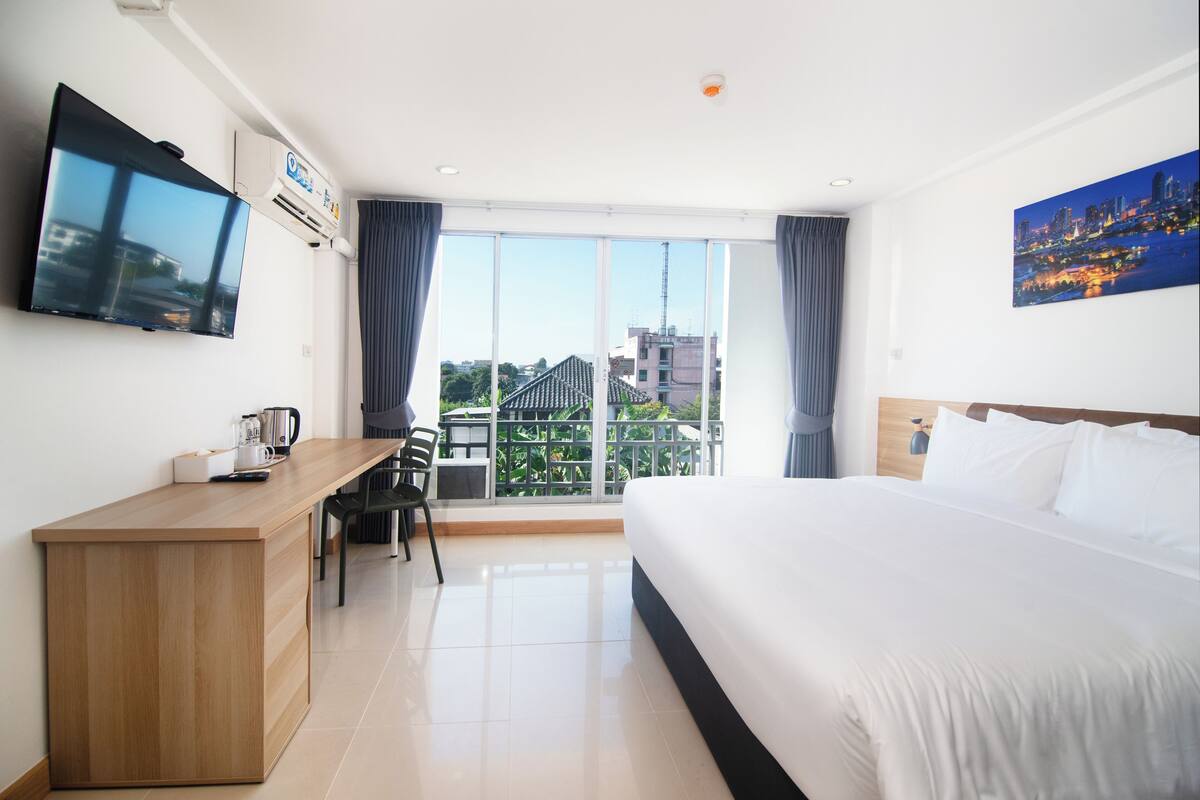Une chambre d’hôtel équipée d’un lit, d’un bureau, d’une chaise, d’un téléviseur à écran plat et d’une grande fenêtre donnant sur la ville.