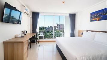 A hotel room with a bed, a desk, a chair, a flat-screen TV, and a large window with a city view.
