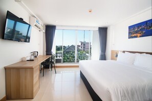 Habitación de hotel con cama, escritorio, silla, televisor de pantalla plana y ventana grande con vista a la ciudad.