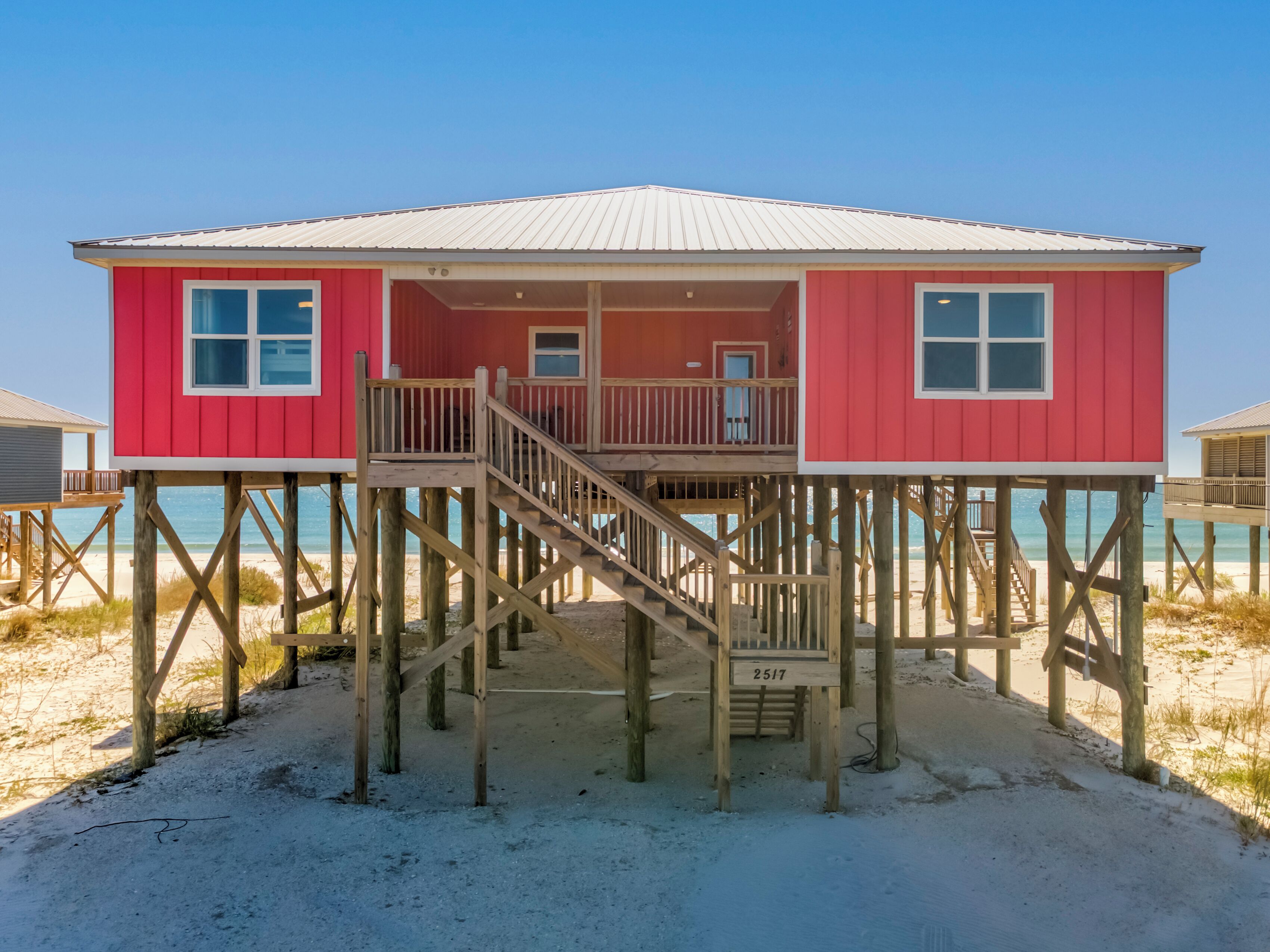 A red wooden beach house with a balcony and a staircase leading to a deck.