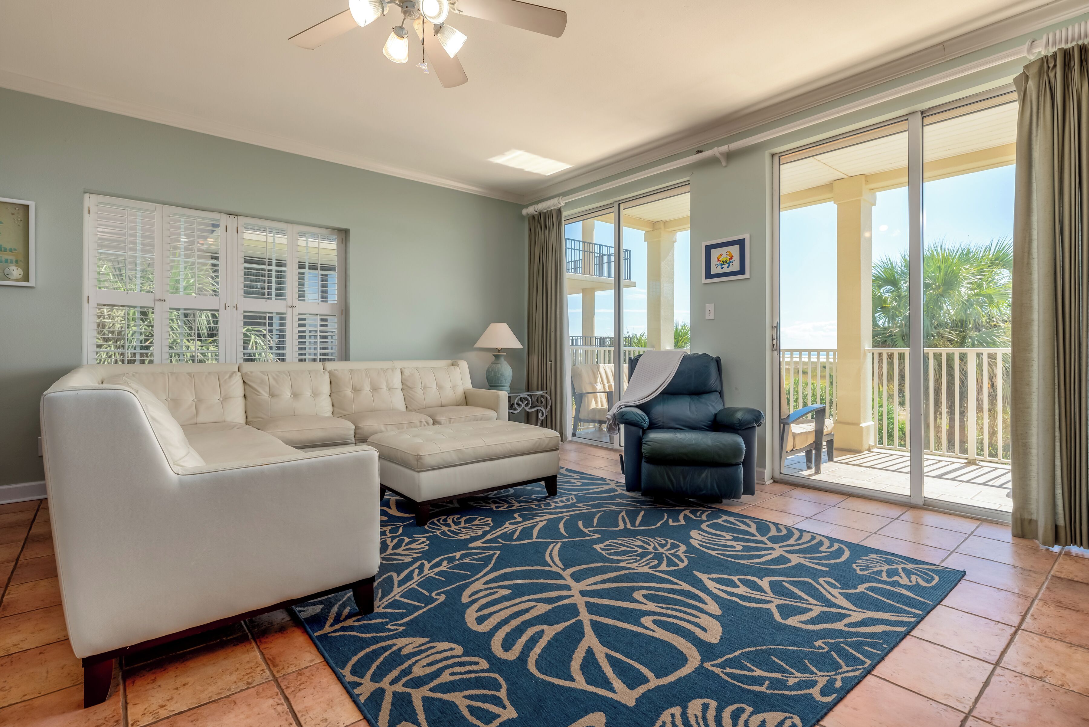 A spacious living room with a white sectional sofa, a dark armchair, and a large blue rug with leaf patterns.