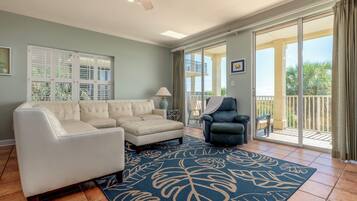 A spacious living room with a white sectional sofa, a dark armchair, and a large blue rug with leaf patterns.