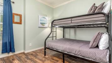 A bunk bed in a room with light green walls, a wooden floor, a framed picture, and a blue curtain.