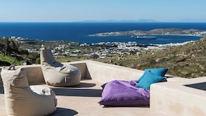 Eine Terrasse mit beigen Sitzsäcken und einem violetten Kissen mit Blick auf eine Küstenstadt und das Meer.