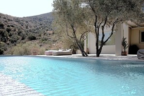 Une piscine avec vue sur une colline et un bâtiment doté d’une grande fenêtre.