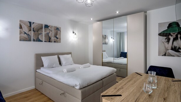 Une chambre à coucher moderne avec un lit, des tables de chevet, une table à manger en bois et des œuvres d’art accrochées aux murs.