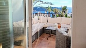 Quarto com porta de vidro deslizante que dá para um espaço de pátio externo com sofá, mesa e plantas em vasos.