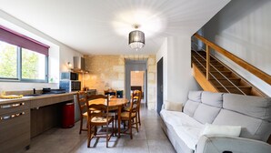 A modern kitchen with a dining table and chairs, a sofa, and a staircase. - Gîte L'Ombrière with Shared Pool, Communal Terrace and Wi-Fi (Saint-Caprais de Bordeaux)