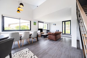 Un salon moderne avec un coin repas, de grandes fenêtres et un escalier.