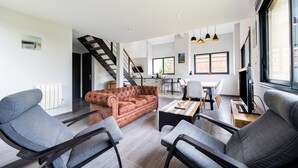 A modern living room with a sofa, chairs, a coffee table, and a staircase leading to a dining area. - Holiday Home 'Gîte Loft' with Shared Pool, Communal Terrace and Wi-Fi (Saint-Caprais de Bordeaux)