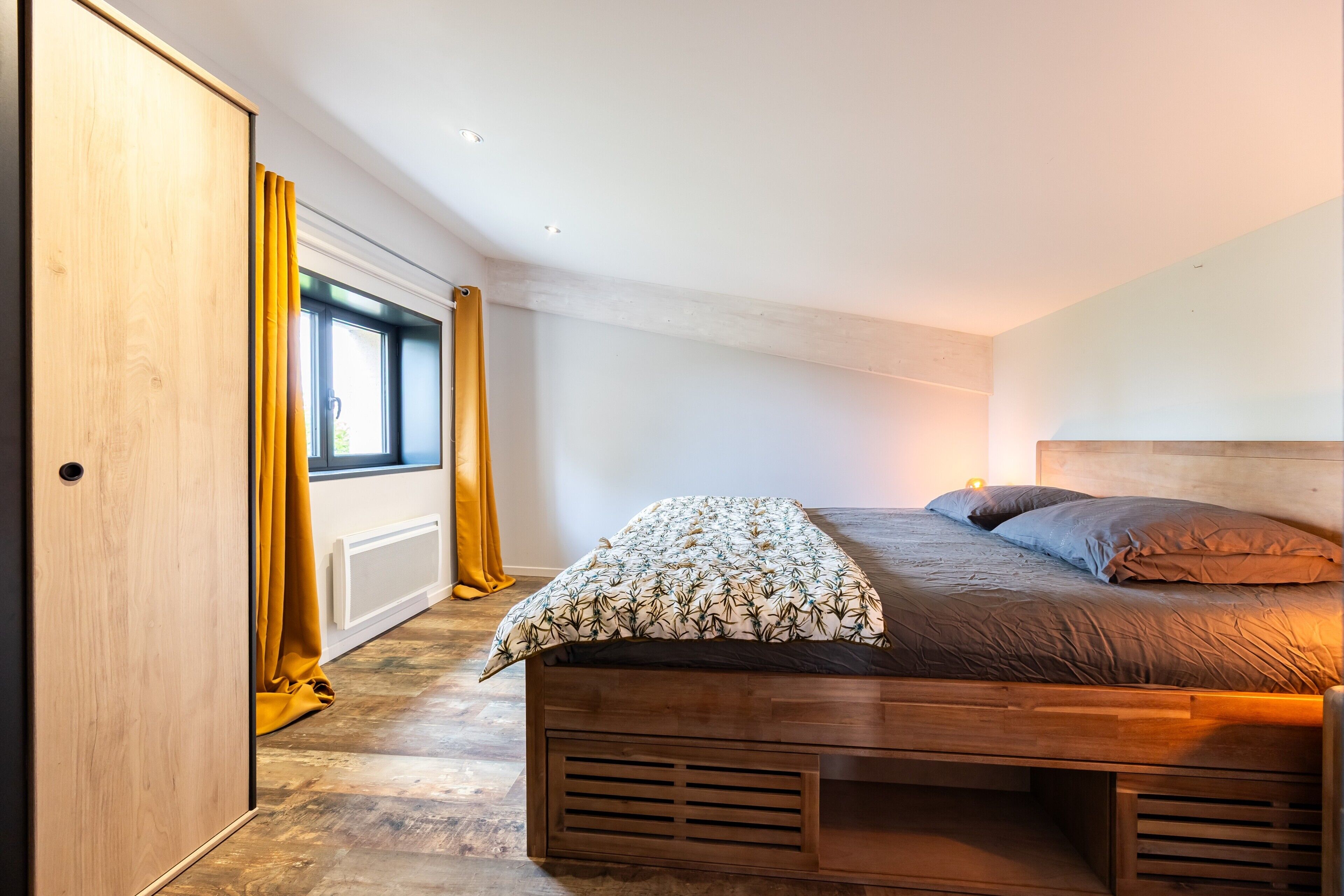 A bedroom with a wooden bed, a window with curtains, and a radiator.