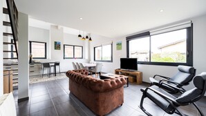 A modern living room with a sofa, a recliner, a TV, and a dining area. - Holiday Home 'Gîte Loft' with Shared Pool, Communal Terrace and Wi-Fi (Saint-Caprais de Bordeaux)