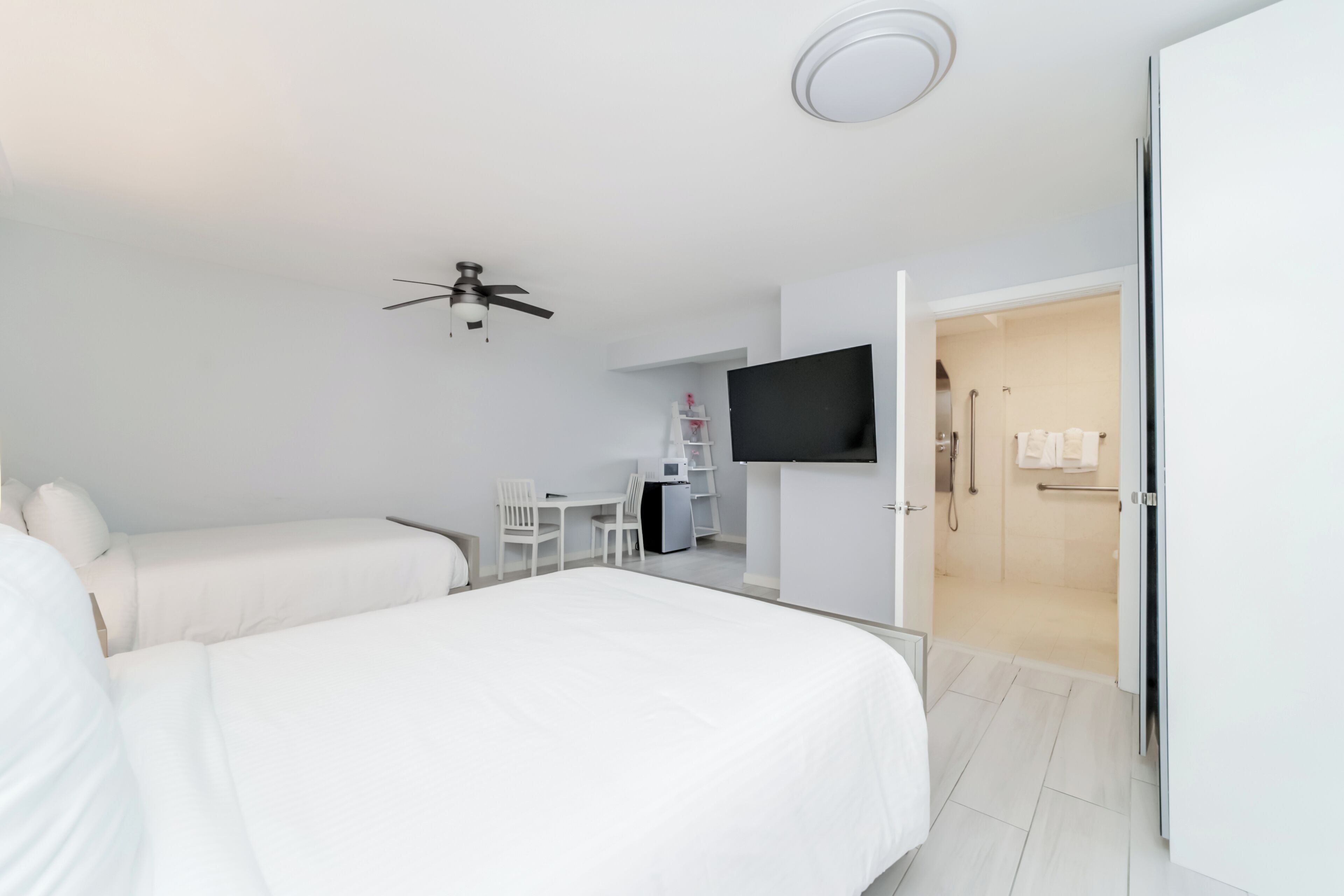 A modern hotel room with a bed, a desk, a chair, a television, and a shower area.