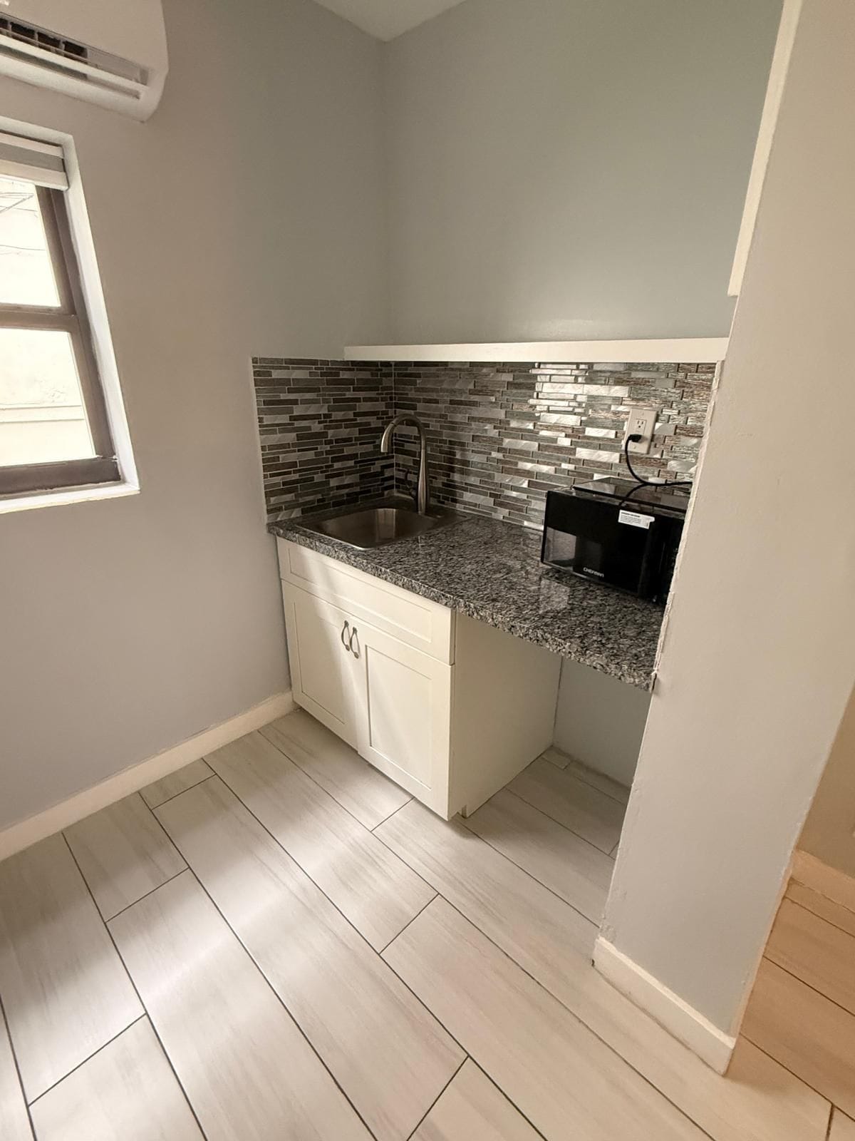 A compact kitchen with a granite countertop, a stainless steel sink, and a tiled backsplash.