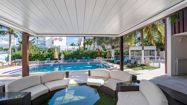 A poolside area with a pool, lounge chairs, and a covered seating area with a view of the cityscape. - Deco Boutique Hotel (Fort Lauderdale)