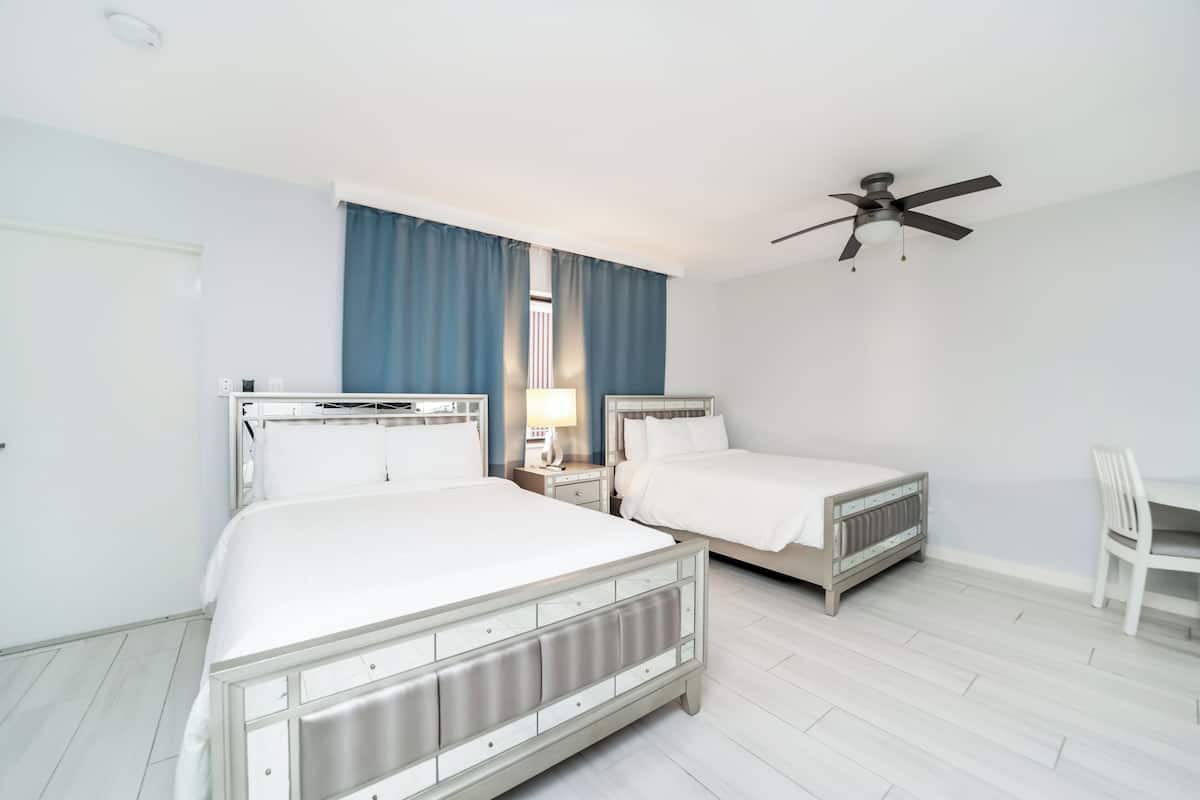 A hotel room with two beds, a ceiling fan, a desk, and a chair.