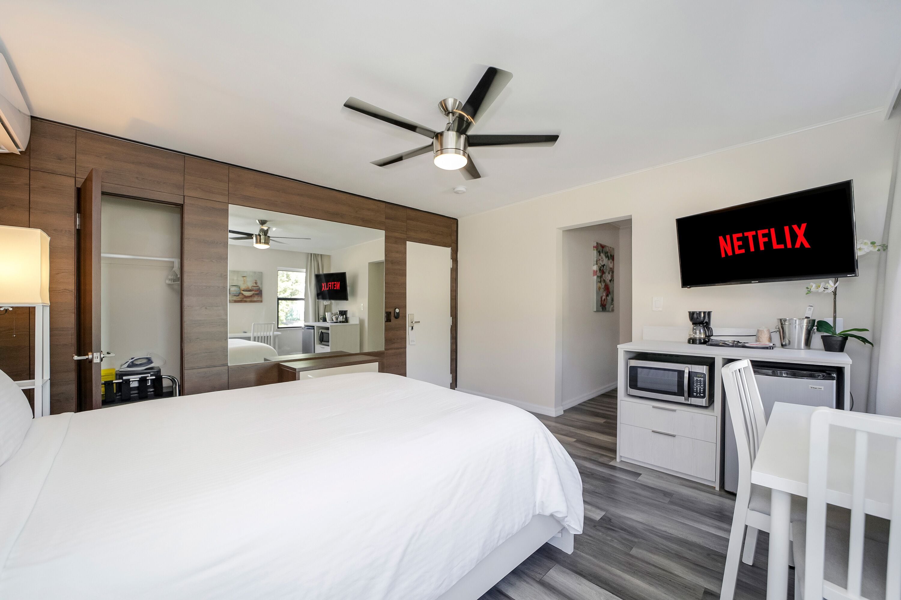 A hotel room with a bed, a desk with a microwave, a TV displaying "NETFLIX", and a ceiling fan.