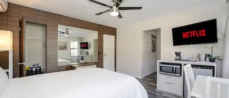 Habitación de hotel con cama, escritorio con microondas, televisor mostrando