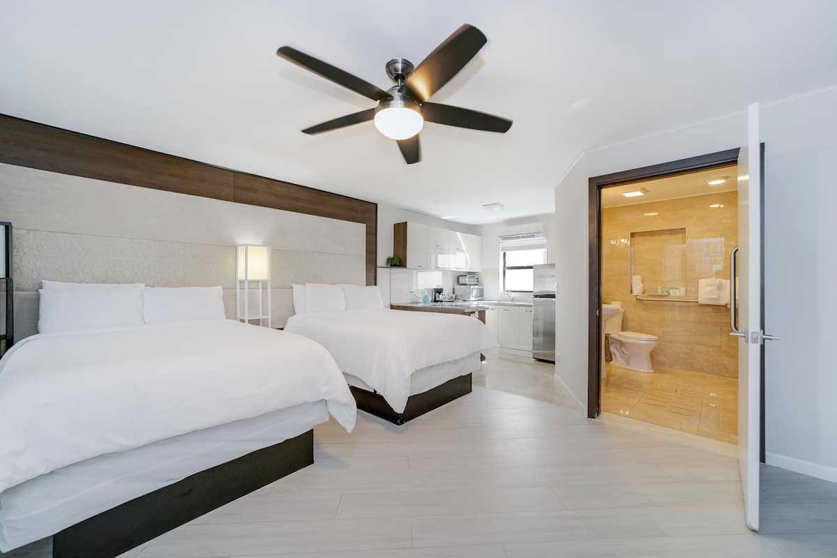 A modern bedroom with two beds, a ceiling fan, and a bathroom visible through an open door.