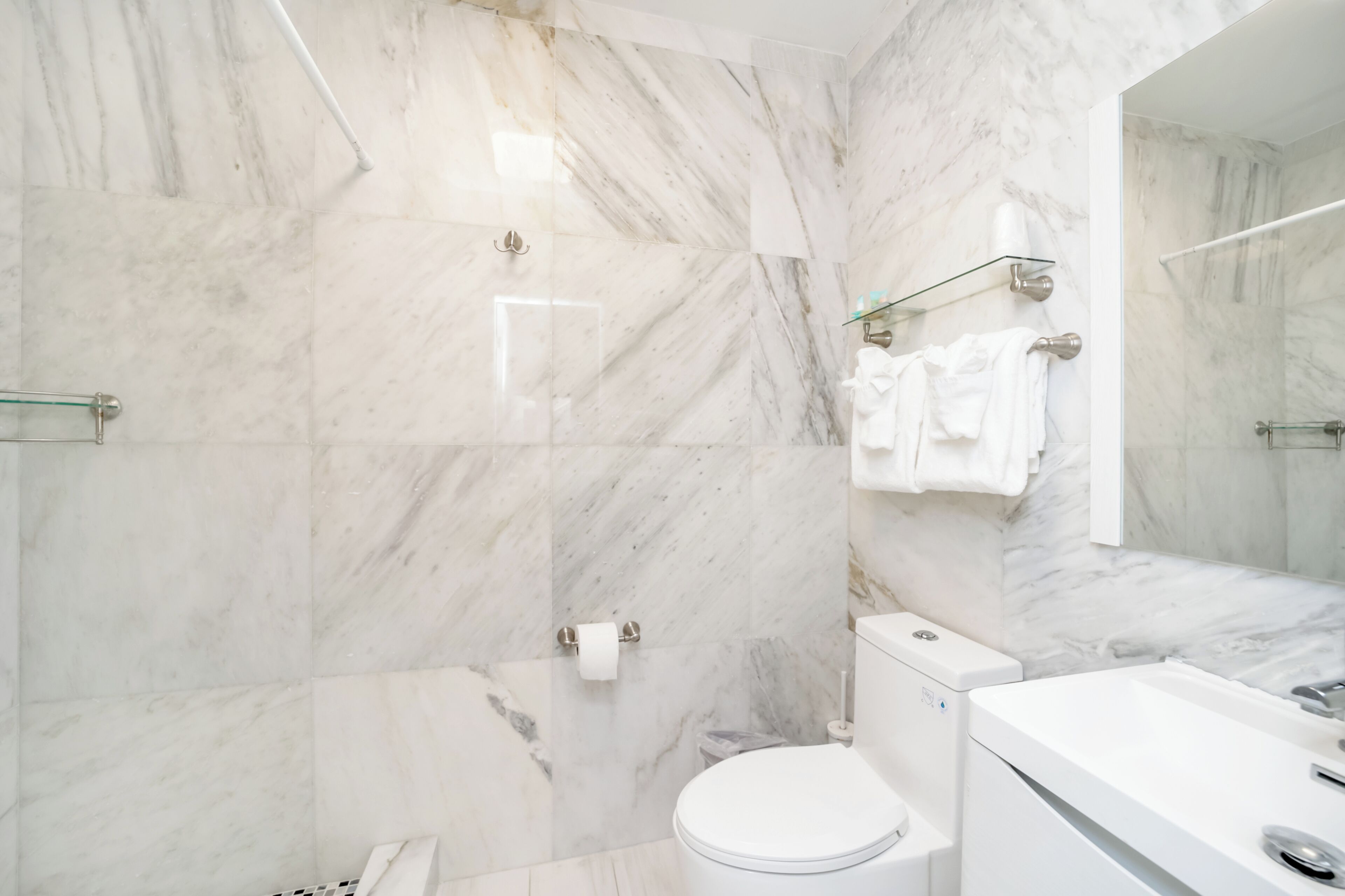 Un baño moderno con paredes de mármol, cabina de ducha de vidrio, inodoro e lavamanos con espejo.