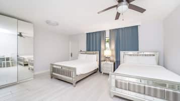 Una camera d'albergo con due letti, una ventola a soffitto, un comodino con una lampada e uno specchio grande.
