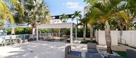 An outdoor seating area with wicker furniture, palm trees, and a covered section.