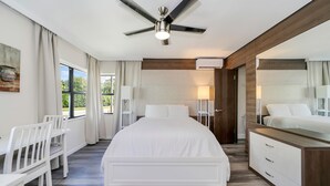 A modern bedroom with a large bed, white furniture, a ceiling fan, and a view of greenery outside. - Deco Boutique Hotel (Fort Lauderdale)