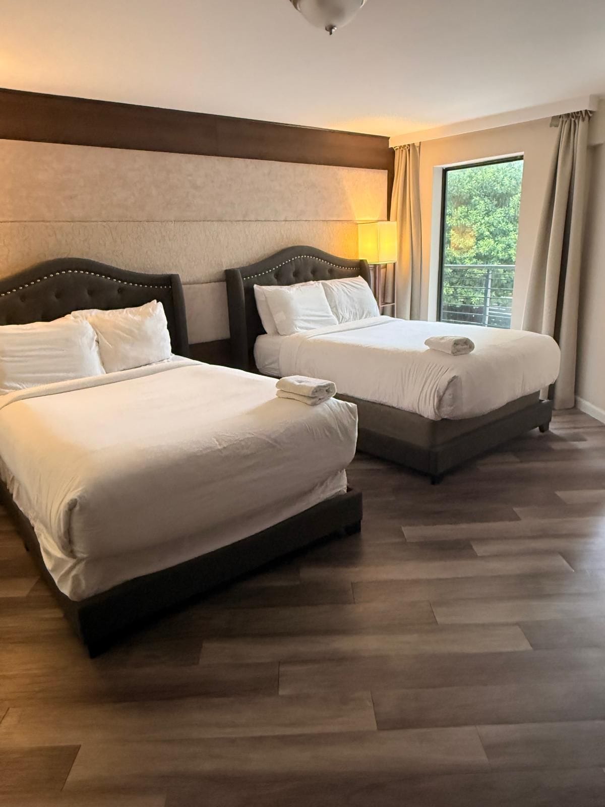 Two beds with headboards, a window with curtains, and a wooden floor.
