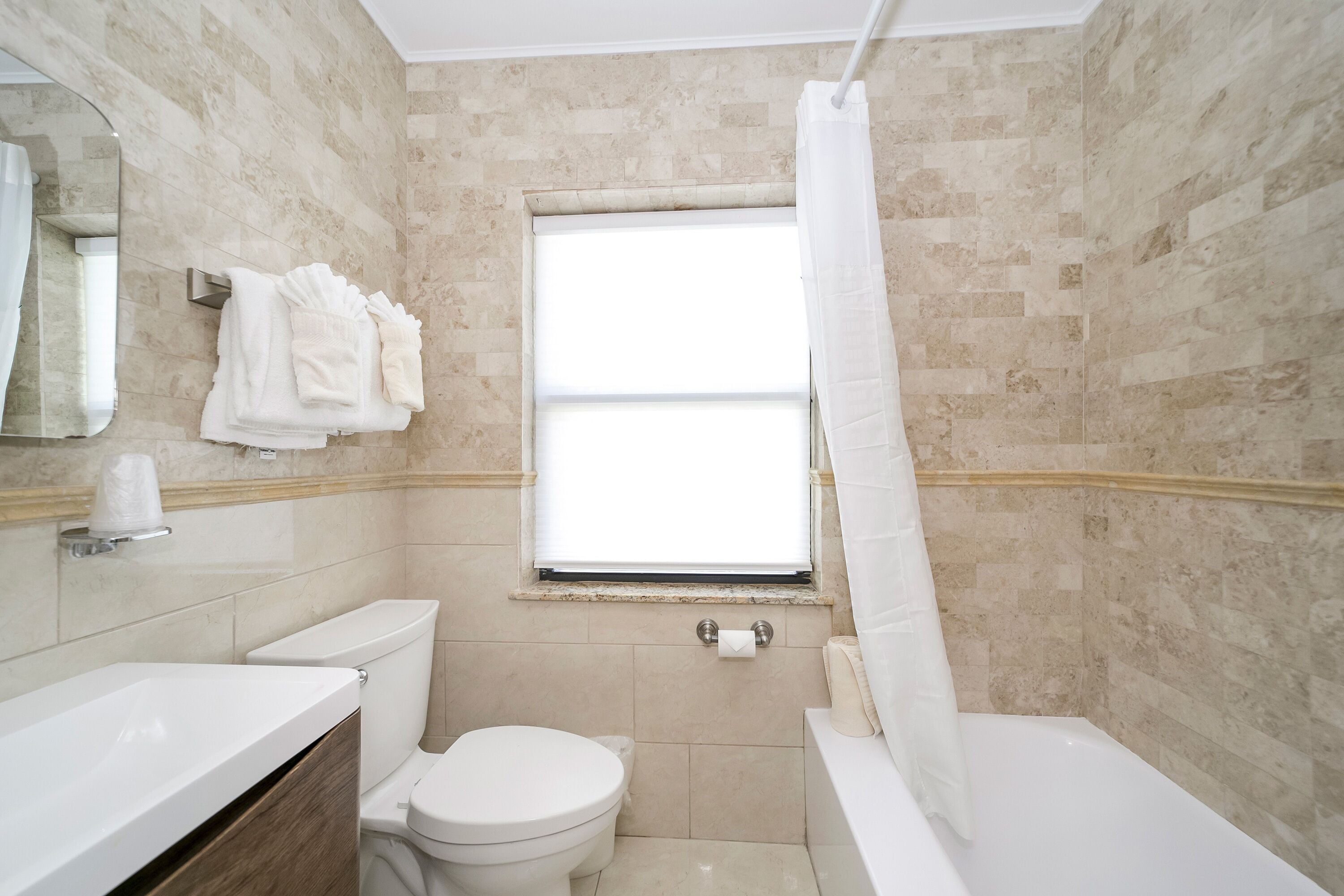 A bathroom with a toilet, sink, and bathtub. There is a window with a curtain, and towels are hung on a rack.