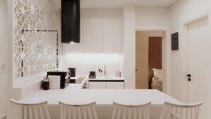 Een moderne keuken met witte kasten, een zwarte afzuigkap en een witte eettafel met vier stoelen.