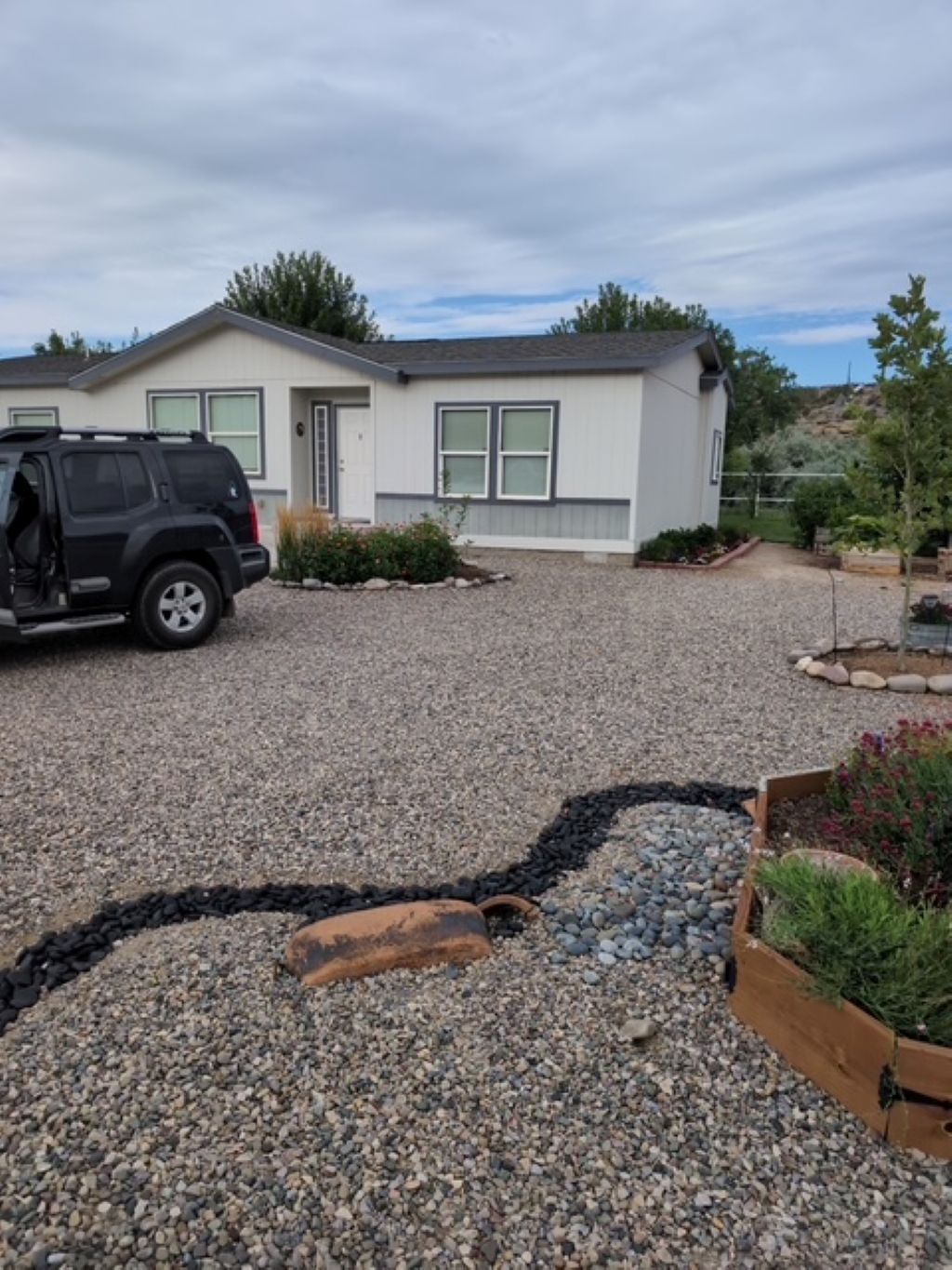 A house with a gravel driveway, a parked SUV, and a garden area with plants.