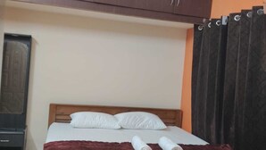 Een slaapkamer met een bed, kussens, een opgerolde handdoek, een houten hoofdbord, een kledingkast en een gordijn.