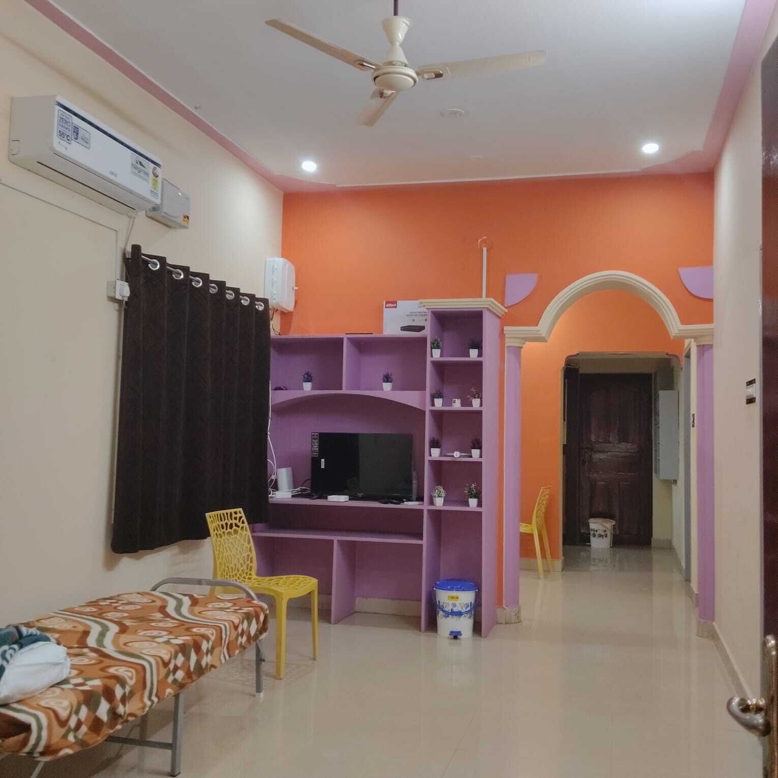 A room with a bed, a TV, a ceiling fan, and a purple shelving unit.