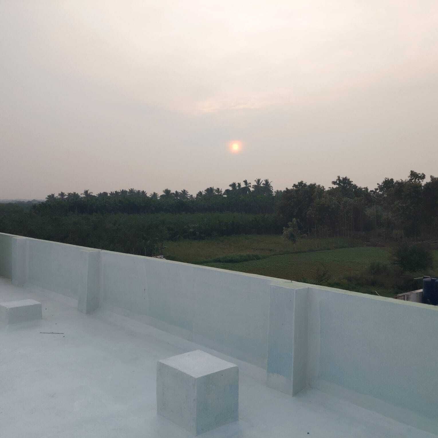A rooftop terrace with a view of a distant landscape and a setting sun.