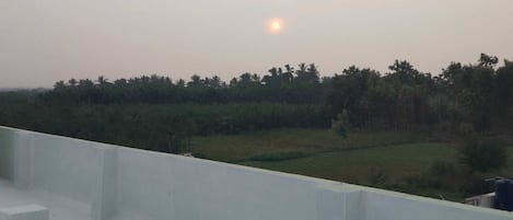A rooftop terrace with a view of a distant landscape and a setting sun.
