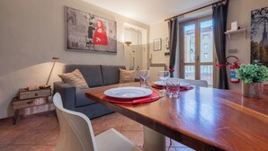 A modern living room with a dining table set for two, a sofa, a side table, and a painting on the wall. - Cozy Flat near Inalpi Arena by Wonderful Italy (Turin)