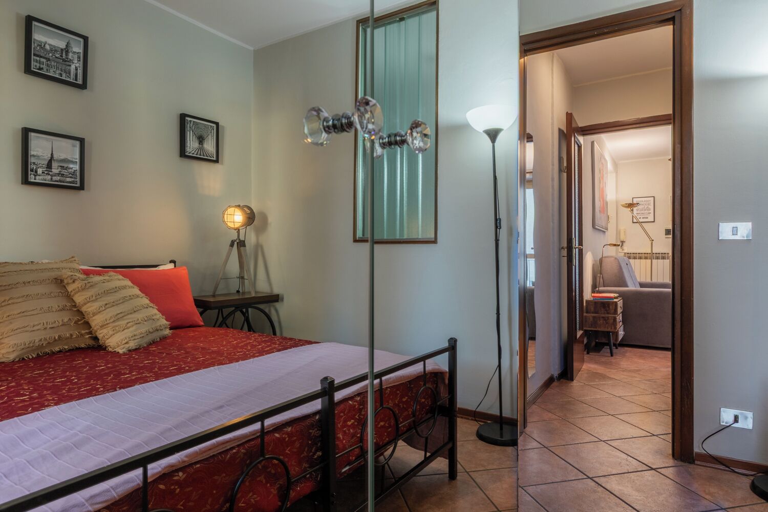 A bedroom with a bed, a bedside table, a floor lamp, and framed pictures on the wall.