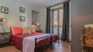 A bedroom with a bed, a nightstand, a lamp, a window with curtains, and a wooden cabinet. - Cozy Flat near Inalpi Arena by Wonderful Italy (Turin)