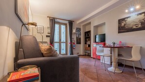 A living room with a sofa, a coffee table, a bookshelf, a TV, and a dining area with chairs and a table. - Cozy Flat near Inalpi Arena by Wonderful Italy (Turin)