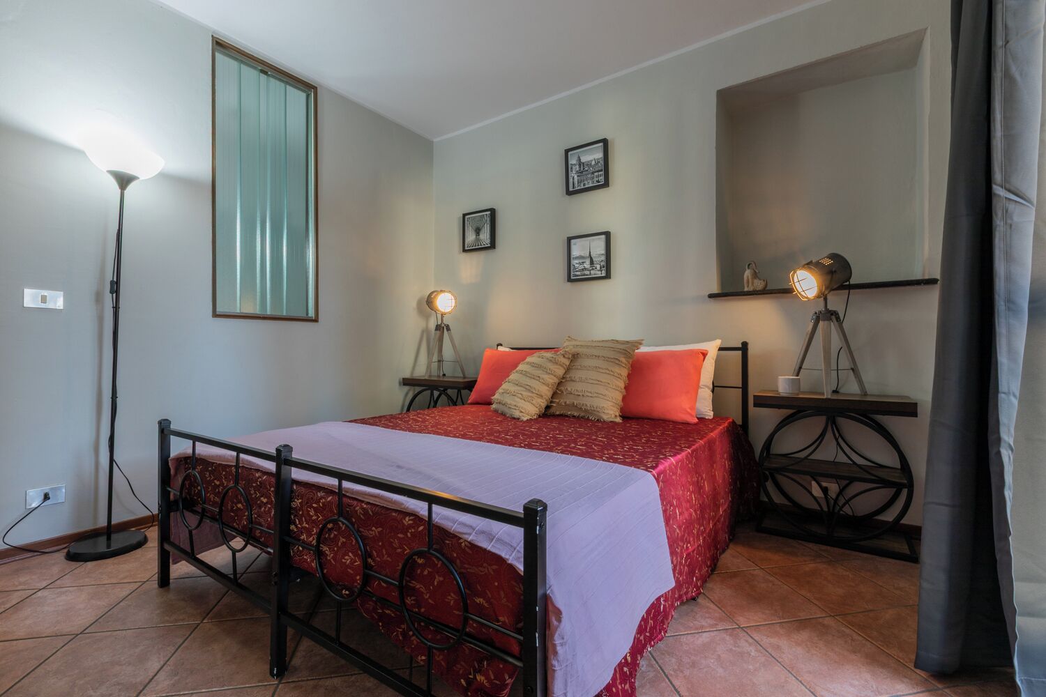 Une chambre à coucher comprenant un lit, deux lampes de chevet, une lampe sur pied et une étagère murale ornée d’une statue.