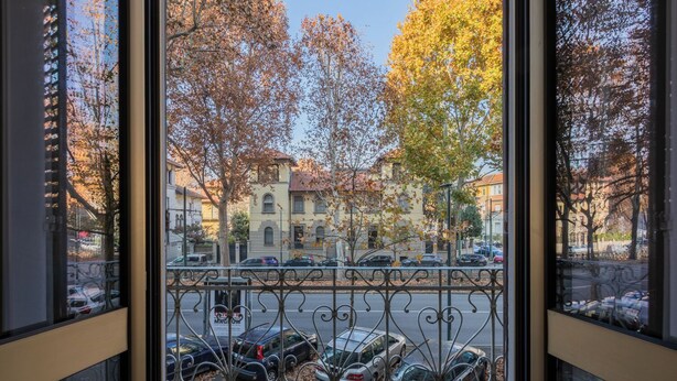 A view through a window with a metal railing, featuring parked cars and autumn trees. - Cozy Flat near Inalpi Arena by Wonderful Italy (Turin)