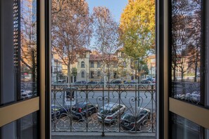 Blick durch ein Fenster mit einem Metallgeländer, zeigt parkende Autos und Herbstbäume.
