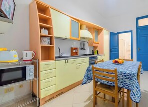 A compact kitchen with a microwave, toaster, and kettle, a dining table with a blue tablecloth, and a blue door.